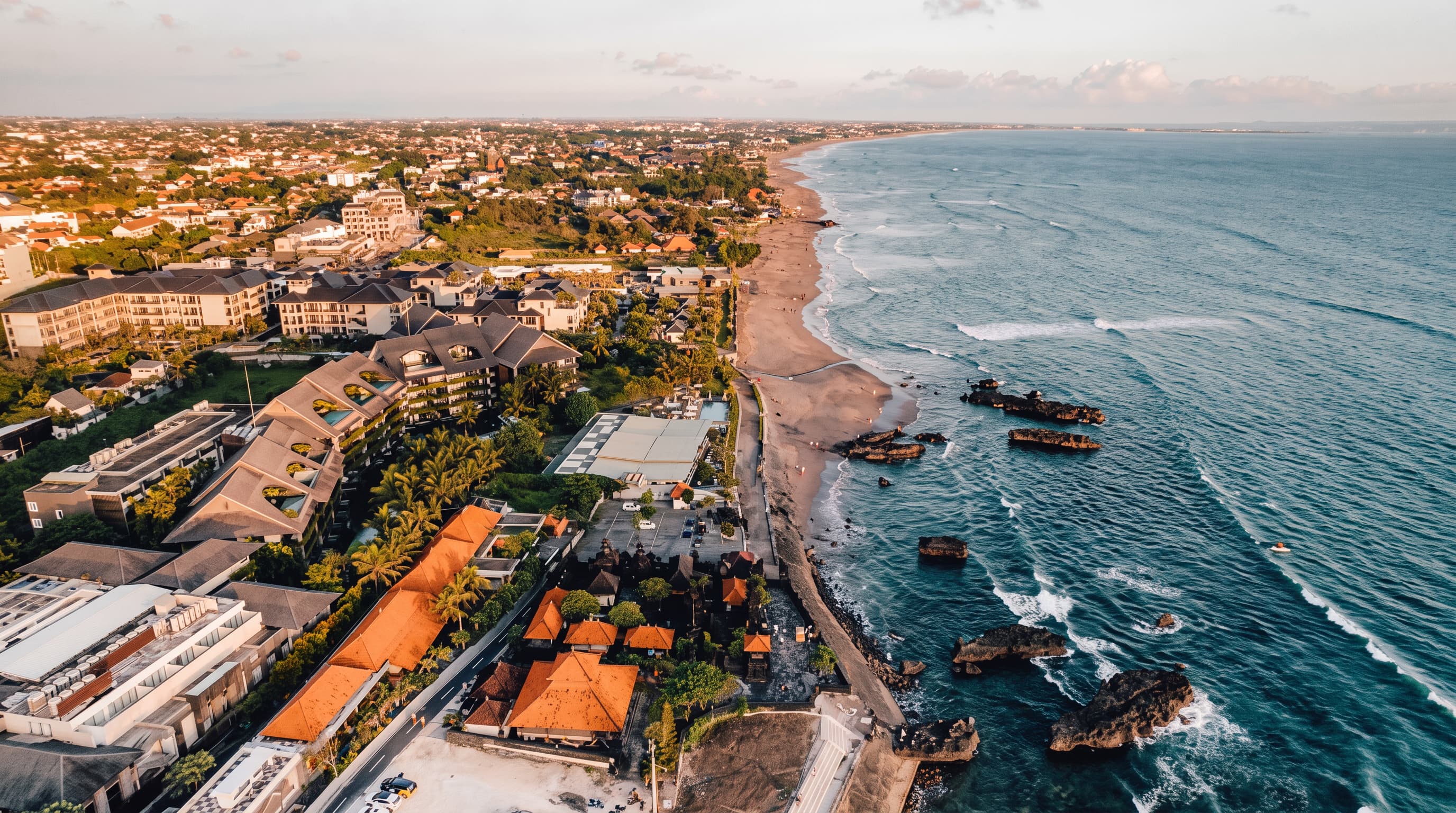 Aerial view of a Bali coastline at golden hour with resorts, palm trees, and surf